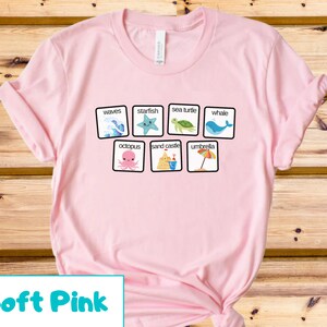 K&ouml;nnte beinhalten: Ein T-Shirt in zartem Rosa mit einer Grafik von Strandmotiven und W&ouml;rtern. Die W&ouml;rter sind "Wellen", "Seestern", "Meeresschildkr&ouml;te", "Wal", "Kraken", "Sandburg" und "Sonnenschirm".