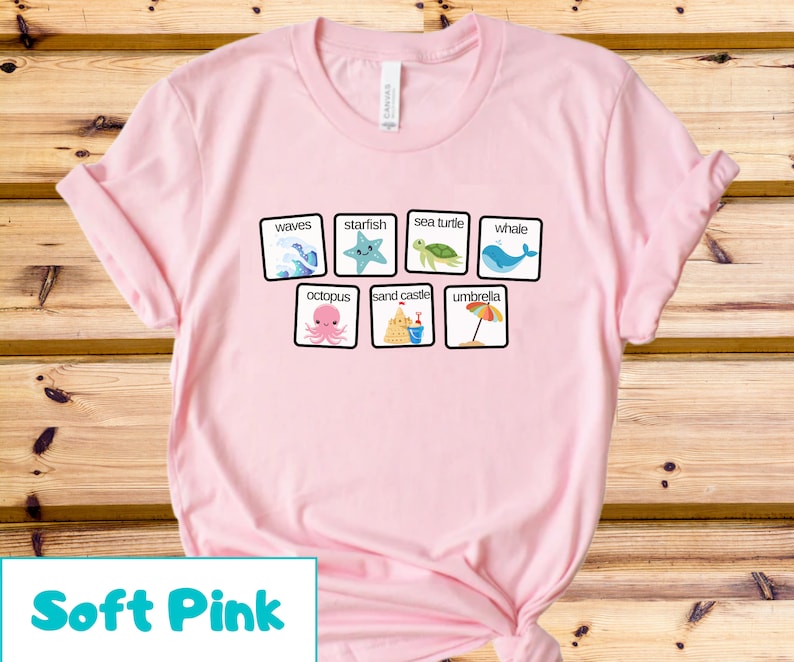 K&ouml;nnte beinhalten: Ein T-Shirt in zartem Rosa mit einer Grafik von Strandmotiven und W&ouml;rtern. Die W&ouml;rter sind "Wellen", "Seestern", "Meeresschildkr&ouml;te", "Wal", "Kraken", "Sandburg" und "Sonnenschirm".