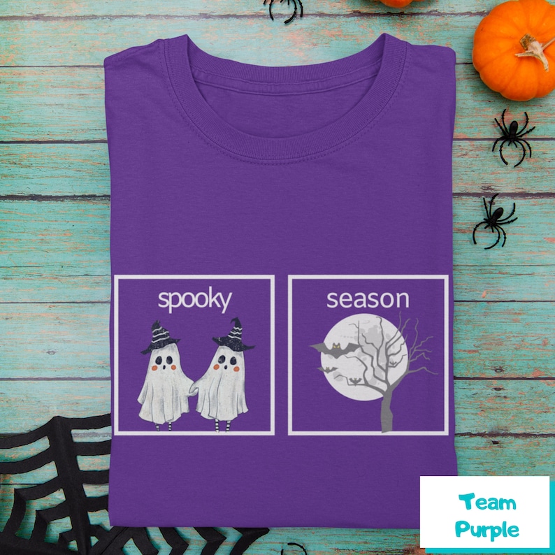 K&ouml;nnte beinhalten: Lilafarbenes T-Shirt mit einer wei&szlig;en Grafik von zwei Geistern mit Hexenh&uuml;ten und dem Text "spooky" und einem Baum mit einer Fledermaus und dem Text "season".