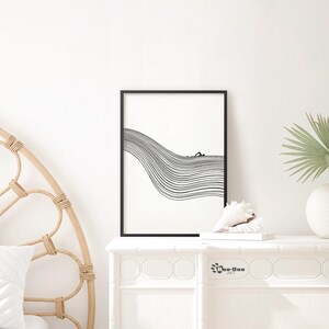 May include: Black and white line art print of a person swimming in a wave. The print is framed in a black frame and is displayed on a white shelf with a seashell and a book.