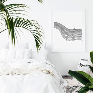May include: A black and white line art print of a person swimming in a wave. The print is framed and hanging on a white wall above a white bed with white bedding. A green plant is in the corner of the image.
