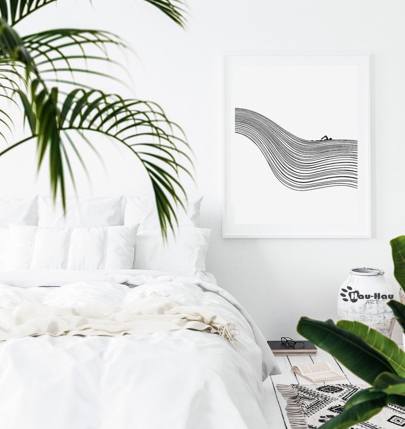 May include: A black and white line art print of a person swimming in a wave. The print is framed and hanging on a white wall above a white bed with white bedding. A green plant is in the corner of the image.