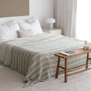 Peut inclure: Un lit avec une literie blanche et une couverture à rayures vertes et blanches. Un petit banc en bois est au pied du lit, et une petite lampe est sur une table de chevet. La pièce a une palette de couleurs neutres.