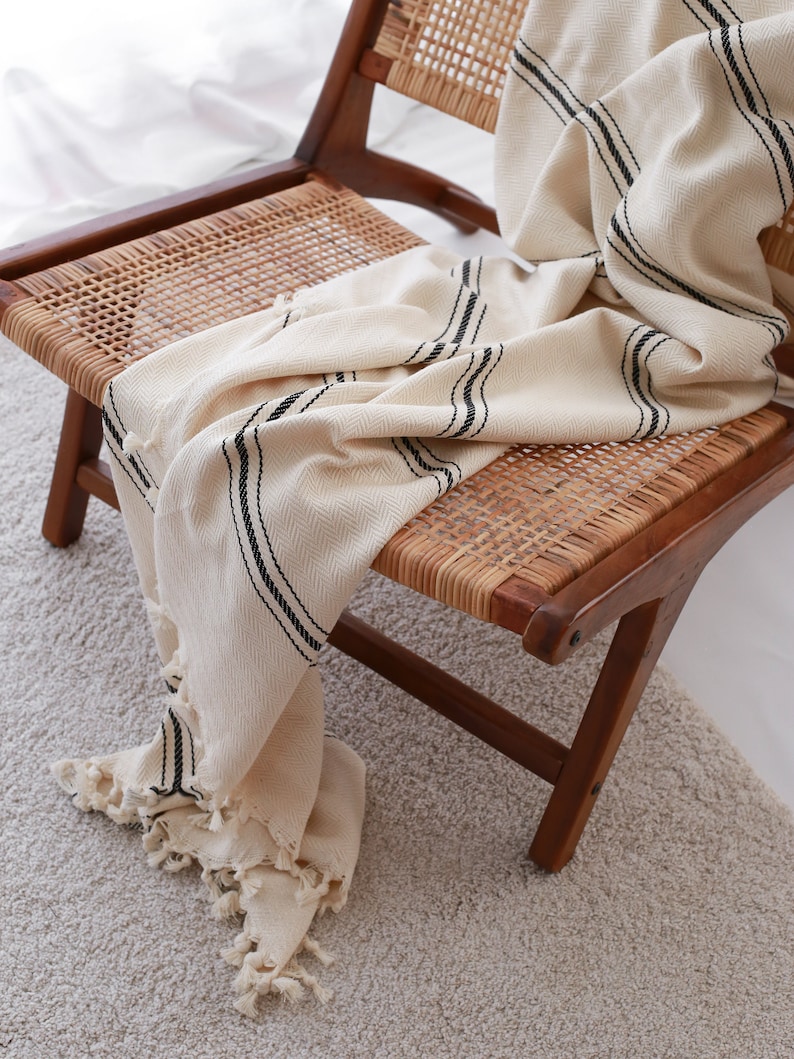 May include: A cream-colored throw blanket with black stripes is draped over a wooden chair with a woven cane seat.
