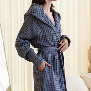 May include: A gray waffle weave bathrobe with a hood and a tie belt. The robe is made of a soft, absorbent material and is perfect for lounging around the house.