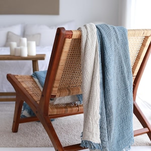 May include: A wooden chair with a woven cane seat and back. A blue and white throw blanket is draped over the back of the chair.