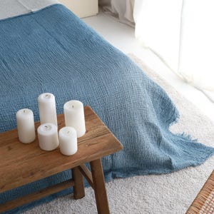 May include: A rustic wooden table with five white candles on top. The table is in front of a bed with a blue and white blanket.
