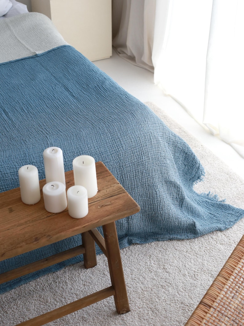 May include: A rustic wooden table with five white candles on top. The table is in front of a bed with a blue and white blanket.