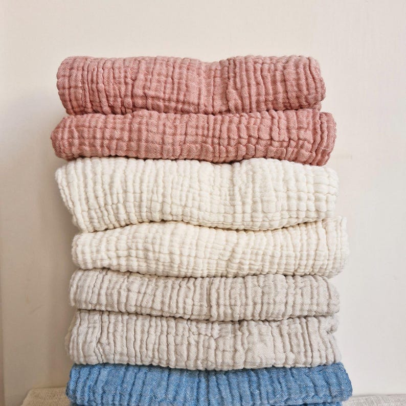 May include: A stack of six soft, textured fabric blankets in various colors, including pink, white, and blue. The blankets are folded and stacked on top of each other.