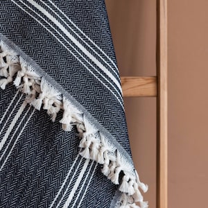 May include: A navy blue and white striped throw blanket with a herringbone pattern. The blanket has white fringe along the edge. The blanket is draped over a wooden ladder.