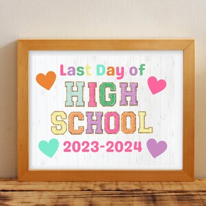 Puede incluir: Una impresión enmarcada con el texto "Last Day of HIGH SCHOOL 2023-2024" en letras coloridas. La impresión tiene un fondo blanco con un patrón de vetas de madera y está decorada con corazones de varios colores. El marco es de madera marrón claro.