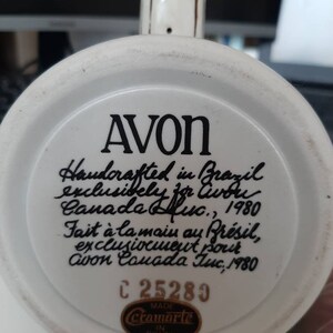 K&ouml;nnte beinhalten: Wei&szlig;e Keramiktasse mit schwarzer Aufschrift: "AVON Handcrafted in Brazil exclusively for Avon Canada Inc., 1980 Fait &agrave; la main au Br&eacute;sil, exclusivement pour Avon Canada Inc., 1980 C 25289 MADE cramarte IN BRAZIL"