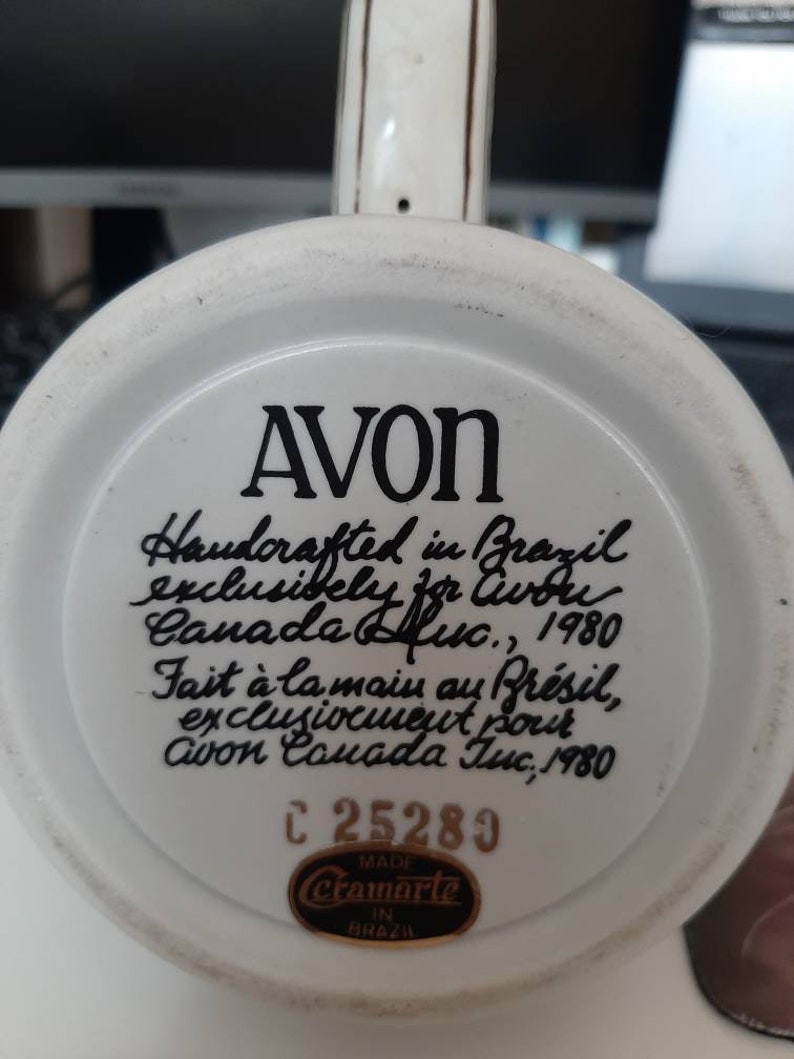 K&ouml;nnte beinhalten: Wei&szlig;e Keramiktasse mit schwarzer Aufschrift: "AVON Handcrafted in Brazil exclusively for Avon Canada Inc., 1980 Fait &agrave; la main au Br&eacute;sil, exclusivement pour Avon Canada Inc., 1980 C 25289 MADE cramarte IN BRAZIL"