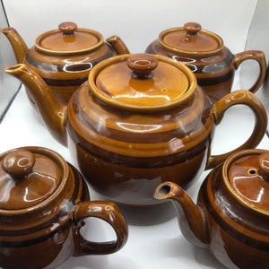 May include: Set of five brown and black striped ceramic teapots with lids. The teapots are all different sizes and have a glossy finish.