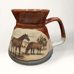 May include: A brown ceramic pitcher with a white handle. The pitcher has a scene of two horses in a field painted on the front.