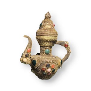 May include: A gold teapot with a decorative lid and a handle. The teapot is adorned with colourful gemstones.