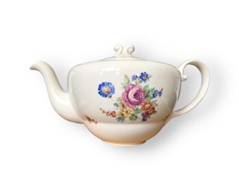 May include: A white teapot with a floral design. The teapot has a lid with a knob on top and a spout on the side. The floral design features pink, yellow, blue, and red flowers.