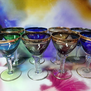 May include: Set of ten vintage stemmed glasses with gold trim. The glasses are in various colours, including blue, green, and purple.