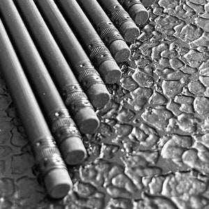 Könnte beinhalten: Ein Schwarz-Weiß-Bild von mehreren diagonal angeordneten Bleistiften. Die Bleistifte haben dunkelgraue Schäfte mit silbernen Metallbändern und angebrachten Radiergummis. Sie liegen auf einer strukturierten Oberfläche.