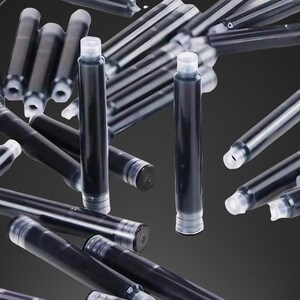 Pu&ograve; includere: Primo piano di un mucchio di cartucce d'inchiostro nero per penne stilografiche. Le cartucce sono in plastica trasparente con un serbatoio d'inchiostro nero. Le cartucce sono sparse su uno sfondo grigio.