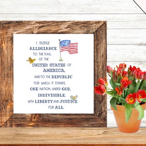 May include: A framed print with the Pledge of Allegiance text in blue and white lettering. The print features a small American flag and two yellow birds. The frame is brown wood with a white mount.