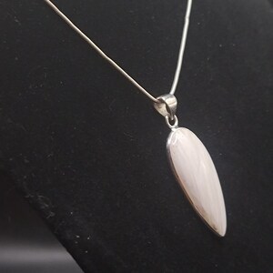 May include: A silver chain necklace with a white oval pendant. The pendant has a subtle swirl pattern.