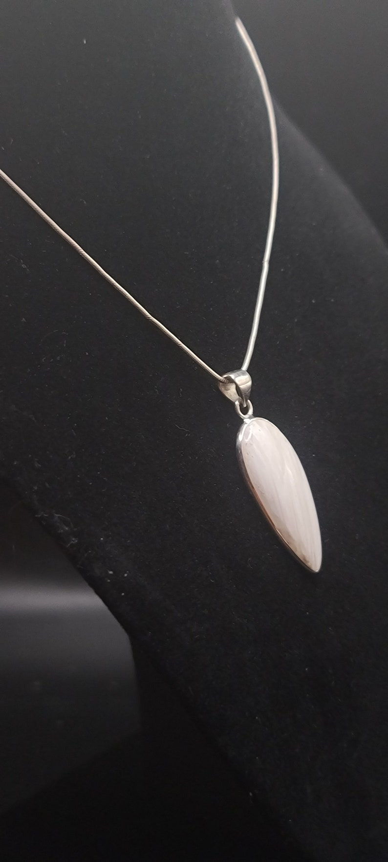 May include: A silver chain necklace with a white oval pendant. The pendant has a subtle swirl pattern.