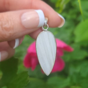 May include: A white teardrop-shaped pendant with a silver bail. The pendant is made of a smooth, white stone with a subtle striated pattern.