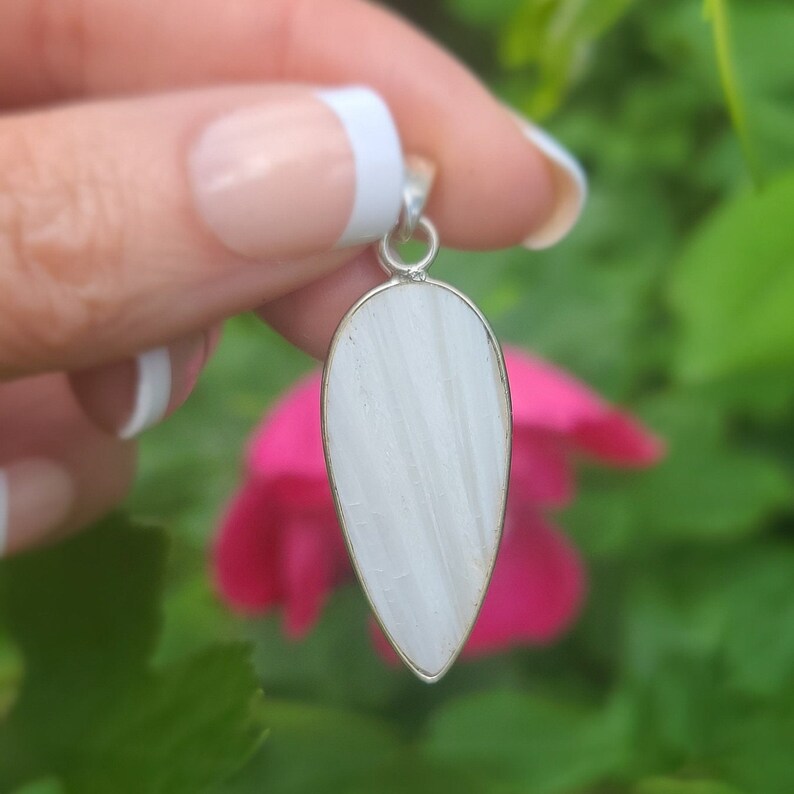 May include: A white teardrop-shaped pendant with a silver bail. The pendant is made of a smooth, white stone with a subtle striated pattern.
