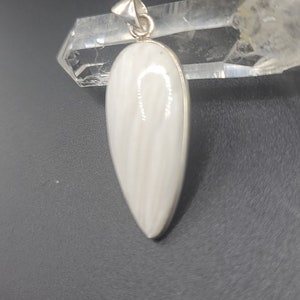 May include: A white teardrop-shaped pendant with a silver bail. The pendant is made of a white stone with a striated pattern.