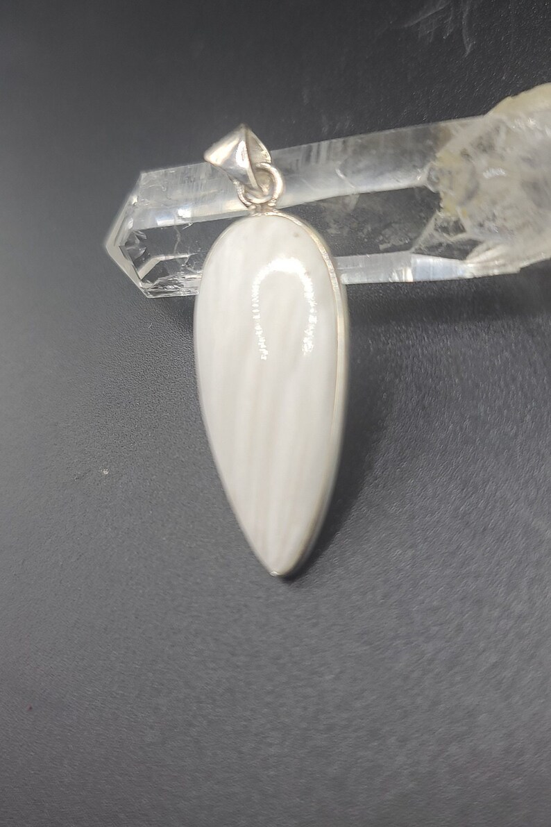 May include: A white teardrop-shaped pendant with a silver bail. The pendant is made of a white stone with a striated pattern.