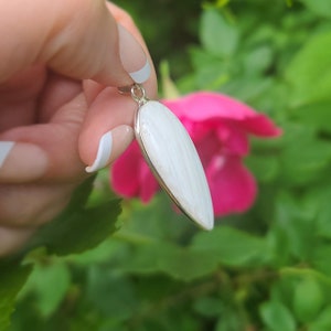 May include: A white, teardrop-shaped pendant with a silver bail. The pendant is made of a natural material with a striated pattern.
