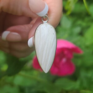 May include: A white teardrop-shaped pendant with a silver bail. The pendant has a striated pattern and is made of natural stone.