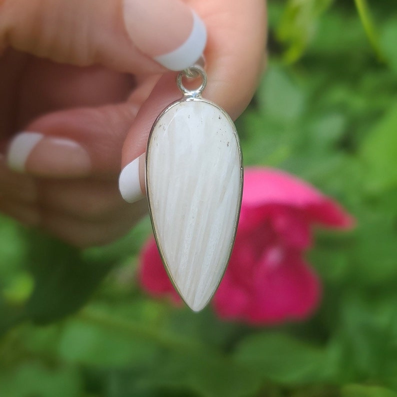 May include: A white teardrop-shaped pendant with a silver bail. The pendant has a striated pattern and is made of natural stone.