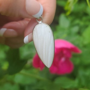 May include: A white teardrop-shaped pendant with a silver bail. The pendant has a striated pattern and is made of natural stone.