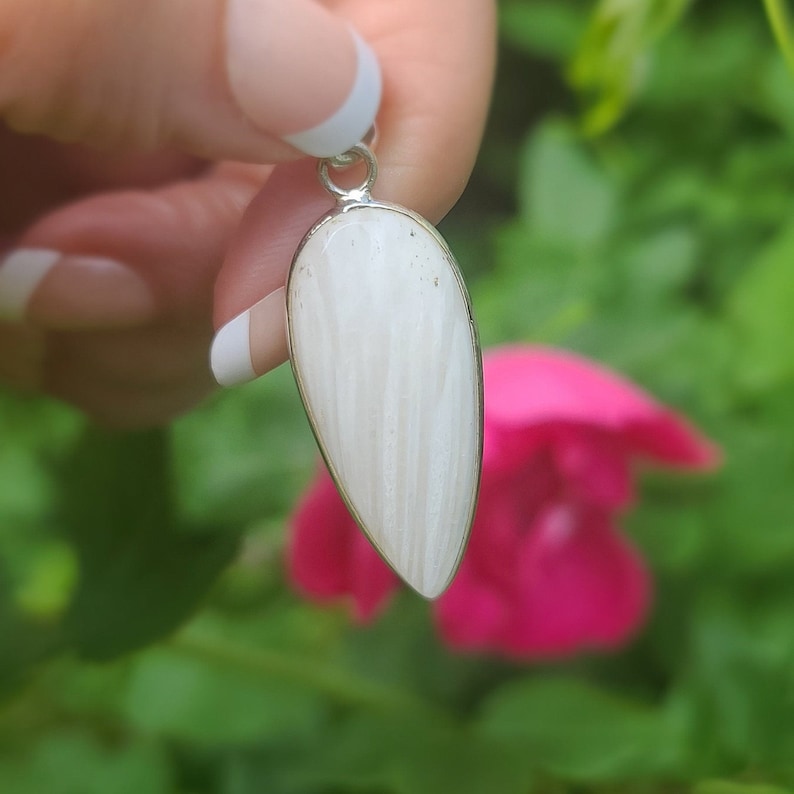 May include: A white teardrop-shaped pendant with a silver bail. The pendant has a striated pattern and is made of natural stone.
