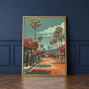 May include: A framed art print depicting a sunny street scene lined with palm trees and buildings. The artwork features a color palette of teal, orange, and pink, with a clear blue sky and fluffy white clouds. The print is displayed on a dark blue wall.