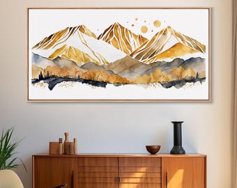 May include: Watercolor painting of a mountain landscape in shades of gold, brown, and blue. The artwork features stylized mountain peaks, a forest, and three golden circles. The painting is framed in a light brown wooden frame.