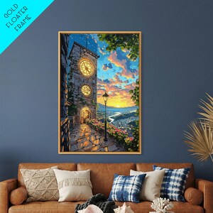 May include: A framed wall art print featuring a stone clock tower with two illuminated clock faces, a cobblestone path, and a vibrant sunset sky over a distant town. The artwork is enclosed in a gold floater frame, displaying a scene with warm orange, yellow, and blue tones, lush green foliage, and a black street lamp.