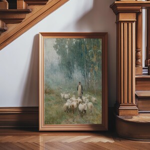 May include: A framed landscape painting depicts a shepherd with a flock of sheep in a forest. The artwork features muted greens and browns, with a light-colored figure in the center. The frame is a light brown color.