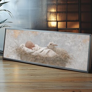 May include: A framed artwork depicts a newborn baby lying in a manger with a lamb. The baby is wrapped in a white cloth, and the lamb is positioned beside the baby. The artwork has a soft, muted color palette.