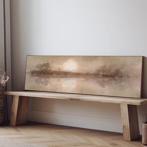 May include: A rectangular landscape painting depicts a serene scene with a reflective body of water, trees, and a figure. The artwork is displayed on a wooden bench. The color palette includes muted tones of brown, beige, and gray.