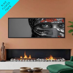 May include: A framed art print featuring a close-up of a person's eyes. The eyes are blue, and the person is wearing a black and white patterned head covering with red accents. The frame is black, and the text "BLACK FLOATER FRAME" is in the upper left corner.