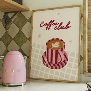 May include: A rectangular framed wall art print featuring a cream background with a grid pattern at the bottom. The centre displays a red and white striped coffee cup on a matching saucer with latte art. The text Coffee club is written in red.