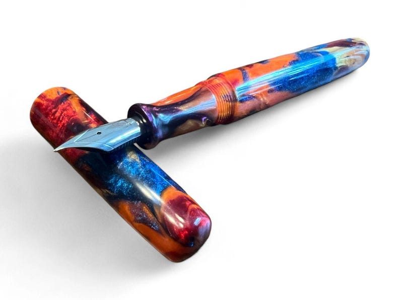 May include: A colorful fountain pen with a blue, orange, and red marbled design. The pen has a silver nib and is lying on its side with the cap off.