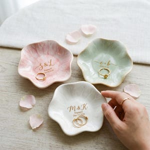 May include: Three scalloped ceramic ring dishes in pastel pink, light green, and white. Each dish features gold-colored text with initials and engagement dates. The pink dish reads S & L Engaged Oct. 10, 2026, the green reads e + b 2026.11.12, and the white reads M & K Engaged Dec. 15, 2026.