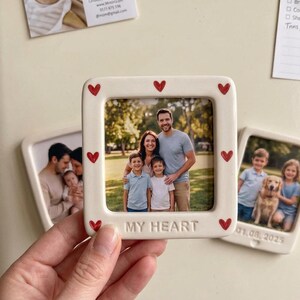 Pode incluir: Uma moldura quadrada de cer&acirc;mica em tom off-white com acabamento brilhante e pequenos cora&ccedil;&otilde;es vermelhos pintados na borda. A moldura tem as palavras MY HEART em relevo na parte inferior e cont&eacute;m uma foto de uma fam&iacute;lia de quatro.