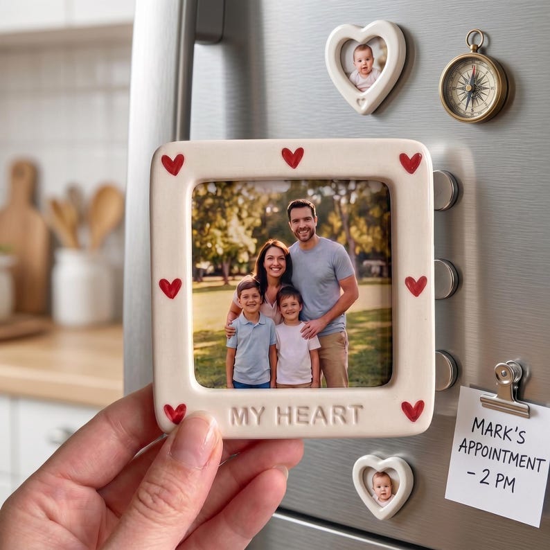 Pode incluir: Uma moldura magn&eacute;tica quadrada de cer&acirc;mica com uma borda cor de creme decorada com pequenos cora&ccedil;&otilde;es vermelhos e o texto em relevo MY HEART. A moldura cont&eacute;m uma fotografia de uma fam&iacute;lia de quatro pessoas numa superf&iacute;cie met&aacute;lica.