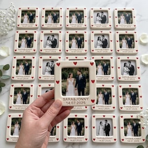 Pode incluir: Uma cole&ccedil;&atilde;o de molduras quadradas de cer&acirc;mica com acabamento branco e pequenos cora&ccedil;&otilde;es vermelhos impressos na borda. Cada moldura cont&eacute;m uma fotografia de um casal e &eacute; personalizada com o texto SARA & JONNY e a data 14.07.2025.