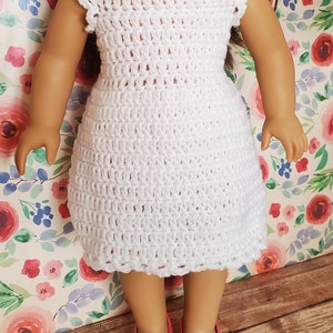 May include: White crocheted dress with a sleeveless design, perfect for a doll. The dress has a simple, elegant style and is made with delicate crochet stitches.
